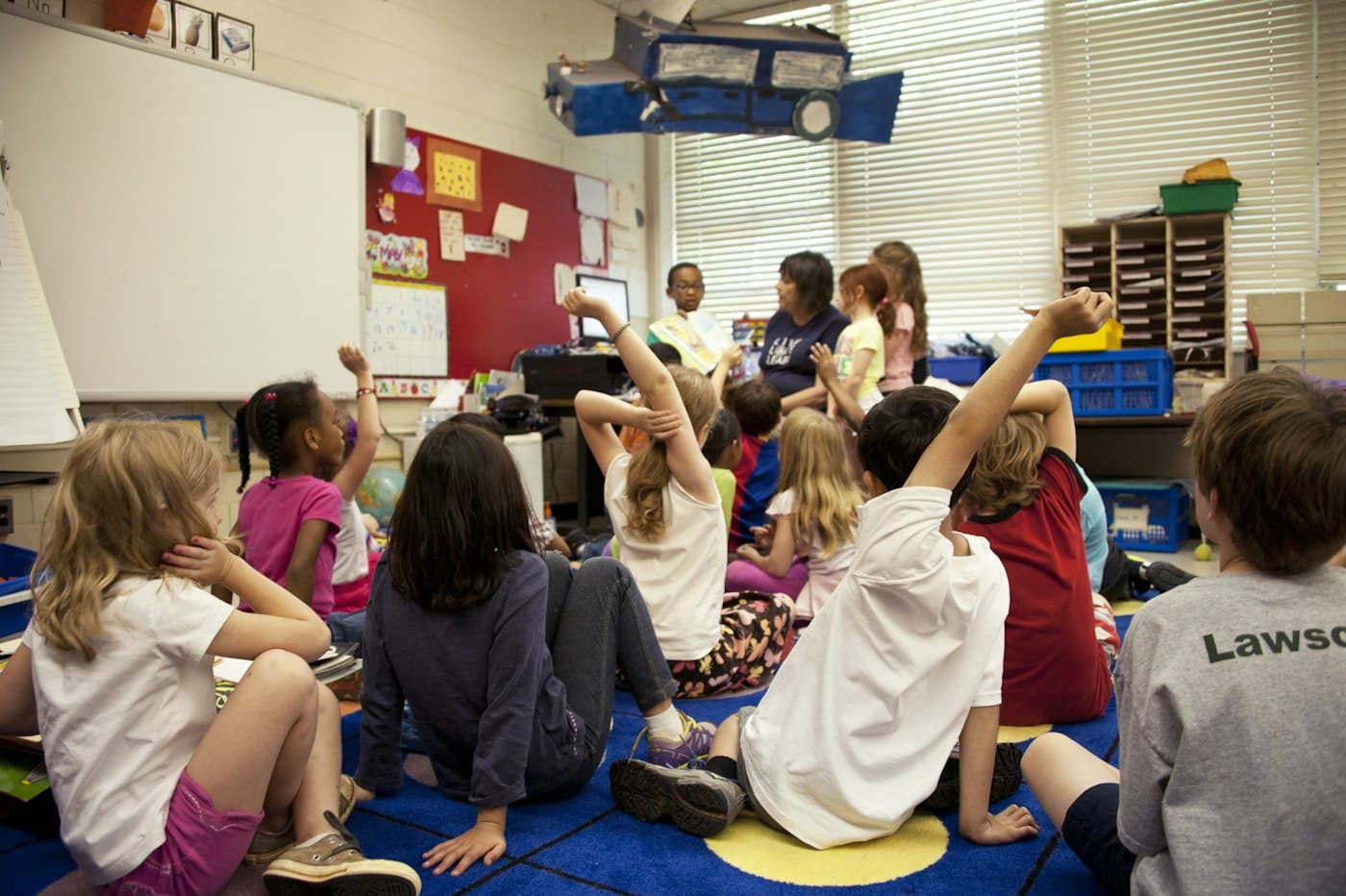 Children gathered on the floor with educators, seen from behind.