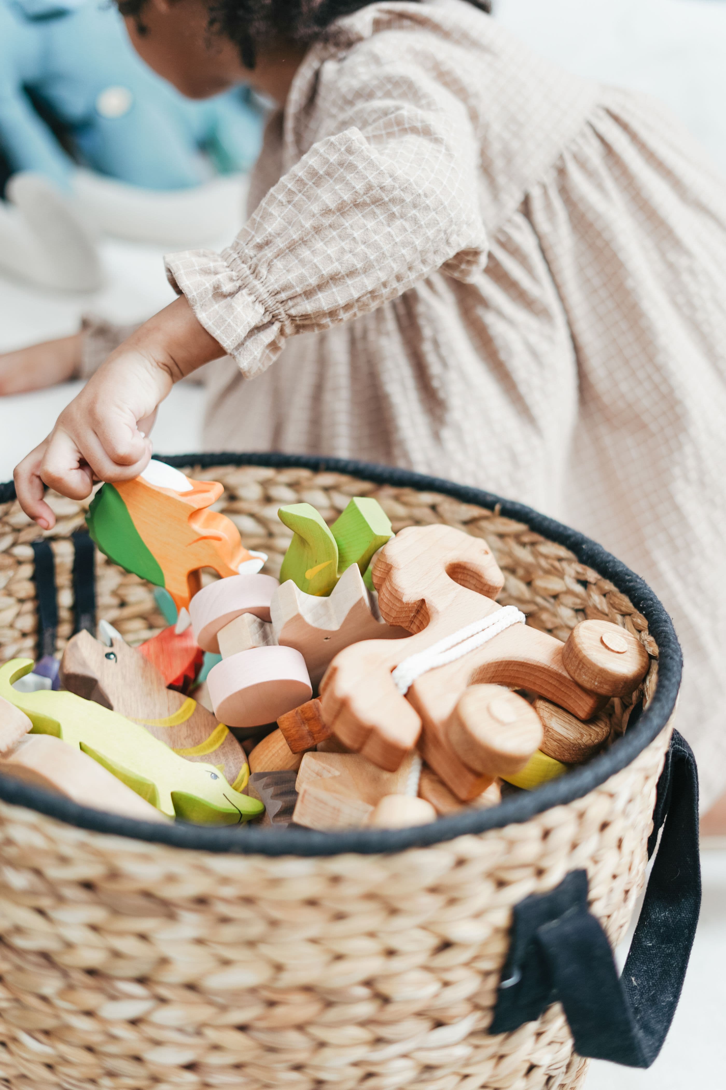 A child reaching into a basket of wooden animals, seen from behind.